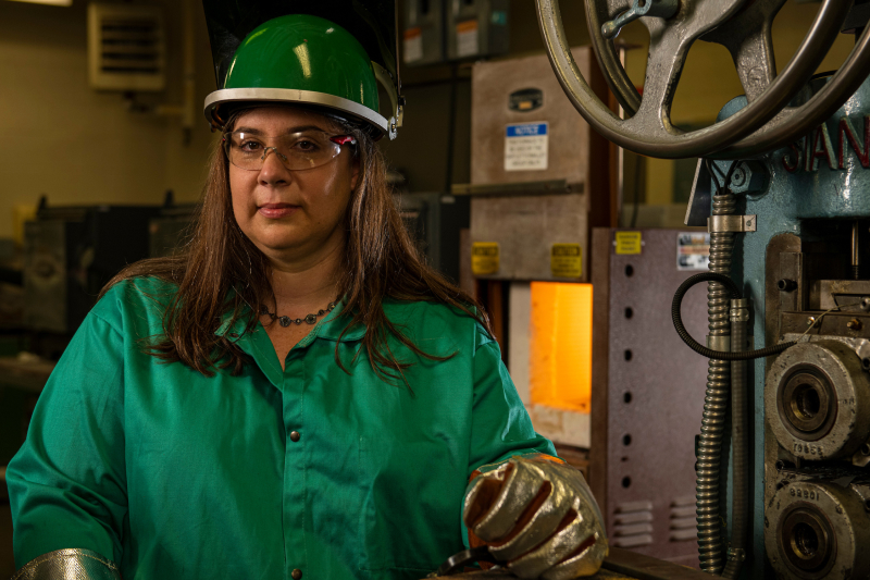 A faculty member stands proudly in heat resistant gear as she heats material in a furnace