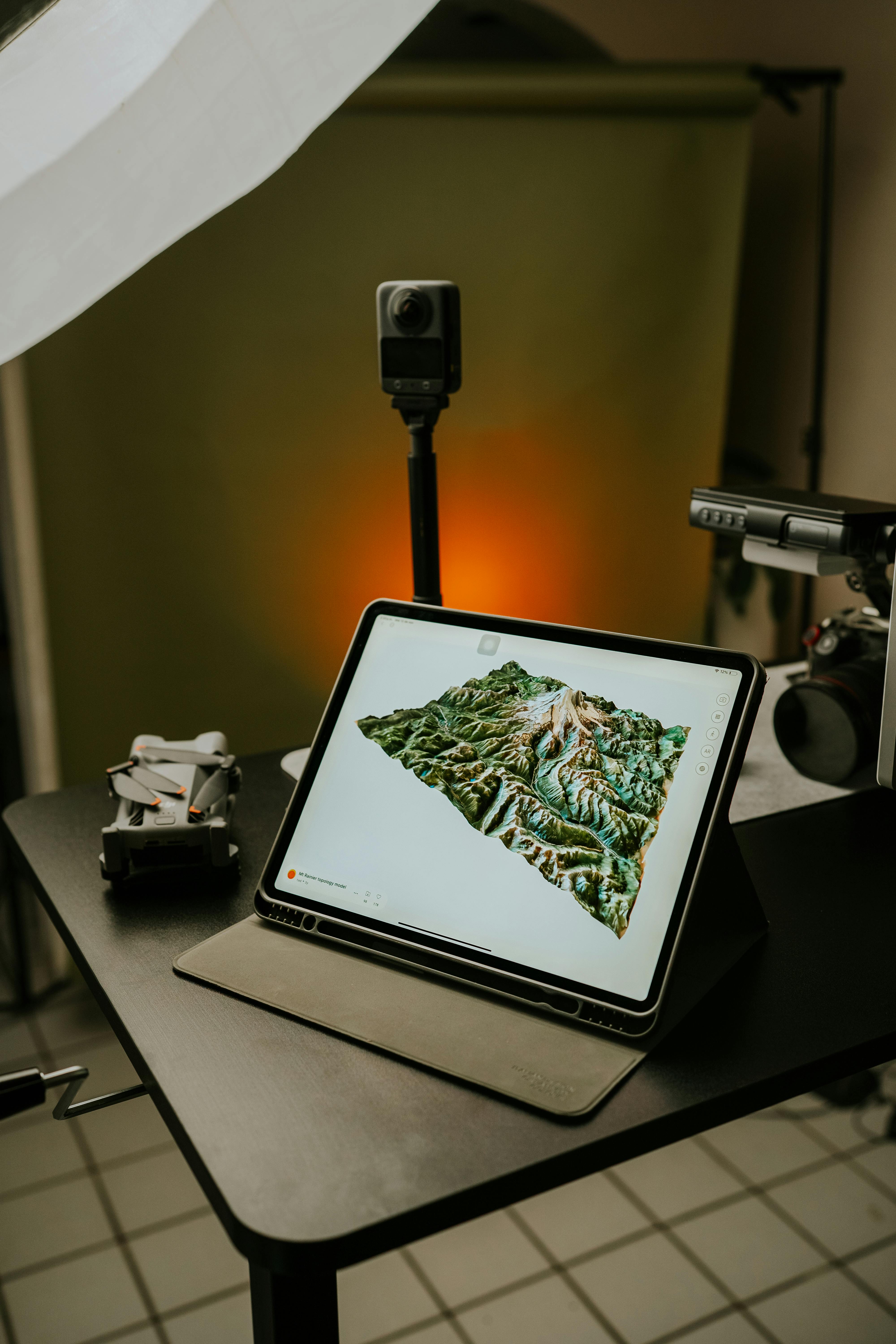 3d topographical map displayed on a laptop which sits next to a drone and camera.