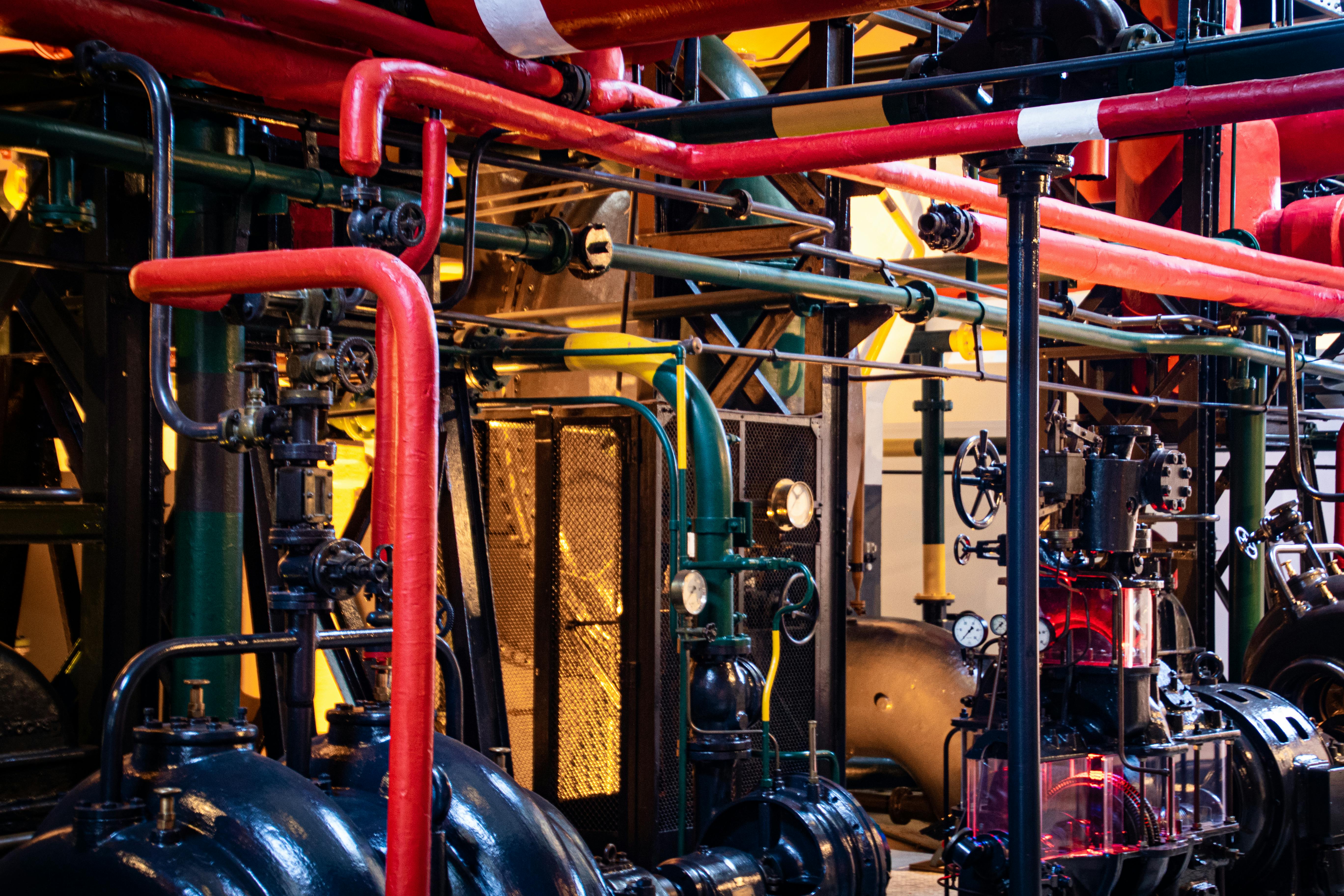 Large machine room containing pipes and valves and machines of different sizes and colors all intersecting one another.
